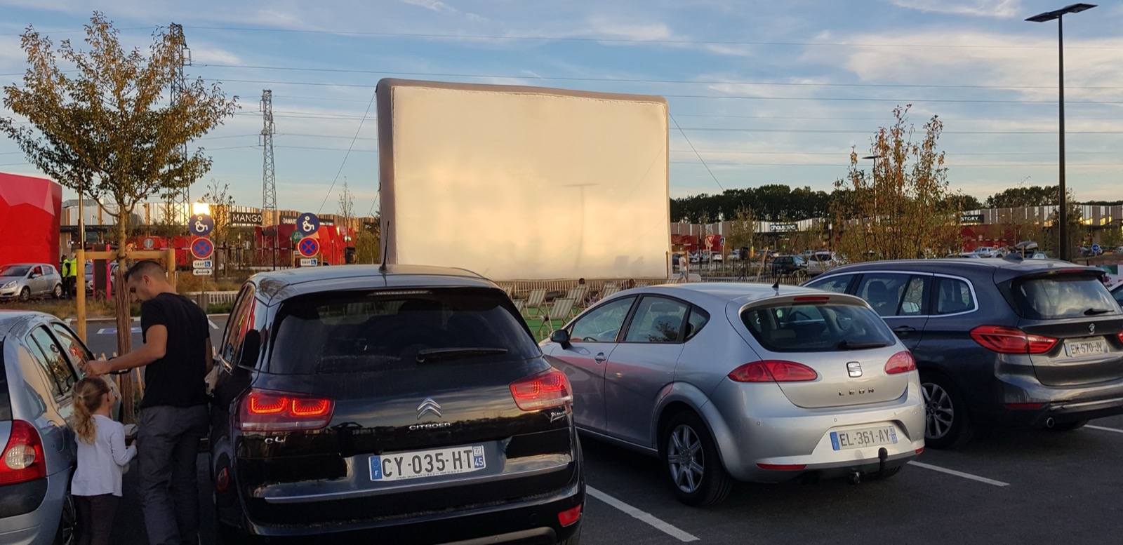 A giant Hallucine inflatable cinema screen set up outdoors, with cars parked nearby